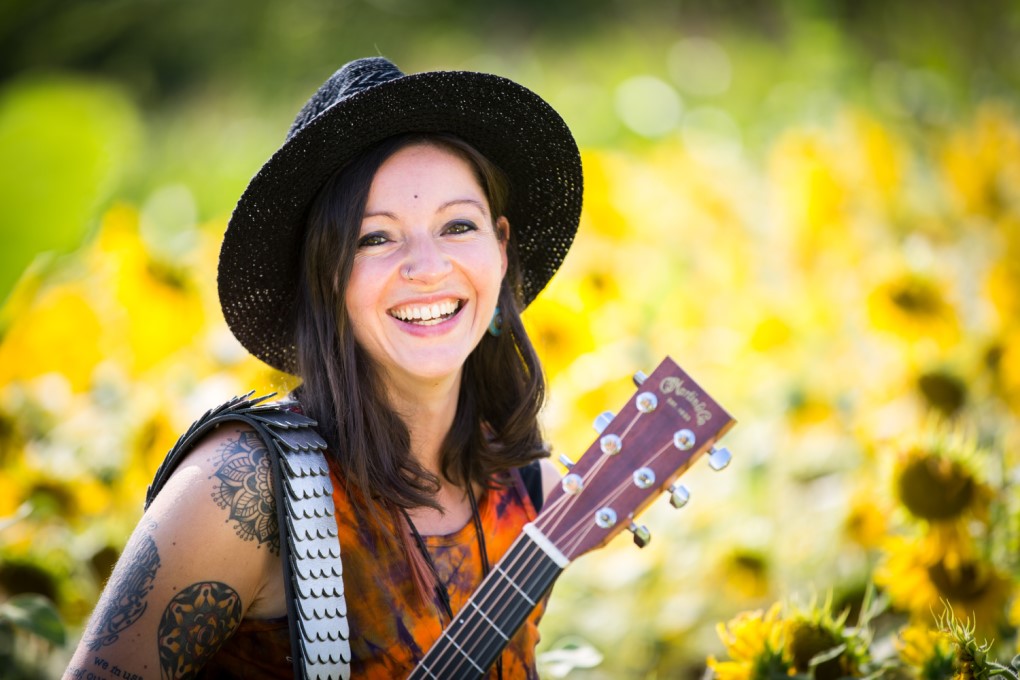 Portrait einer Frau mit Sonnenhut und Gitarre in einem Sonnenblumenfeld