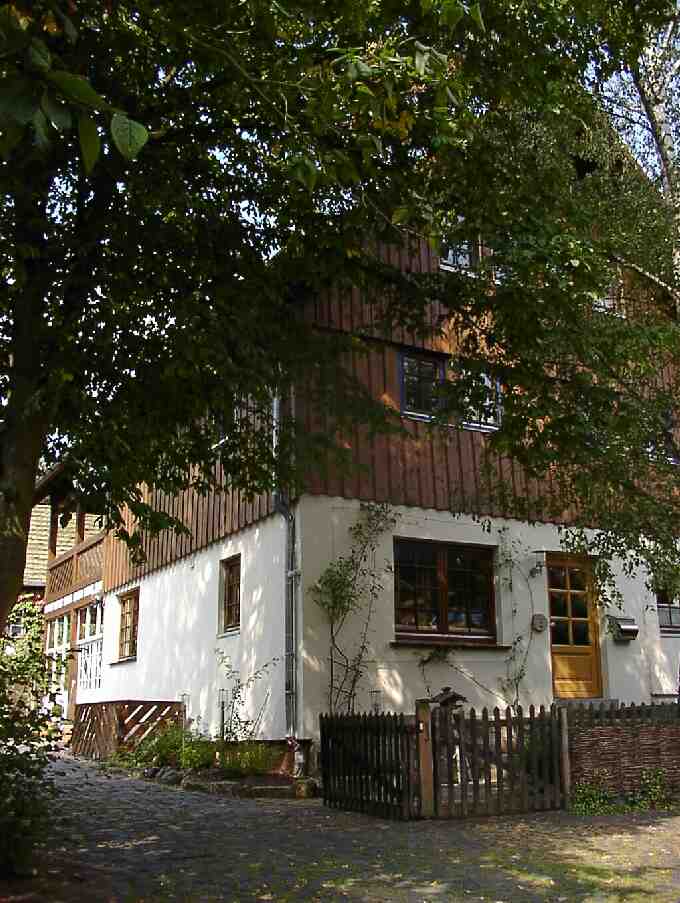 Hinter Bäumen verstecktes Haus mit holzverkleideten Obergeschoss