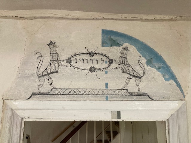 Bemalung auf Putz: Zwei Löwen halten ein Schild mit der hebräischen Inschrift „Ludwig“