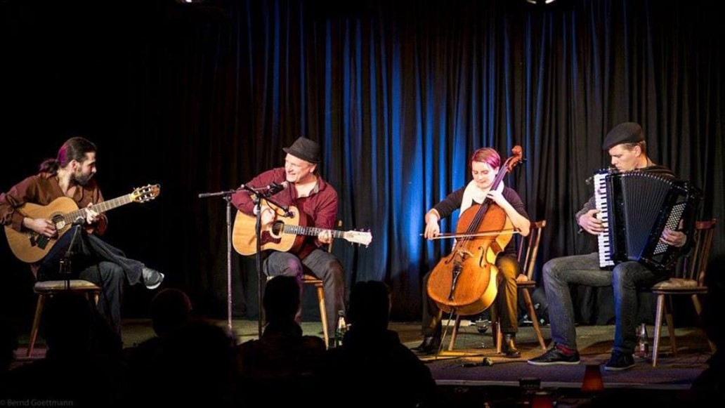 3 Musiker und eine Musikerin mit ihren Instrumenten vor einem blauen Vorhang